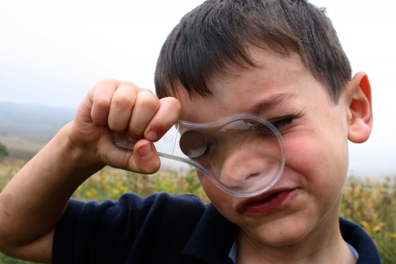 Young boy with magnifying glass smushed against face